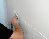 Ręka nakłada sztablatura, tworząc gładź na ścianie.