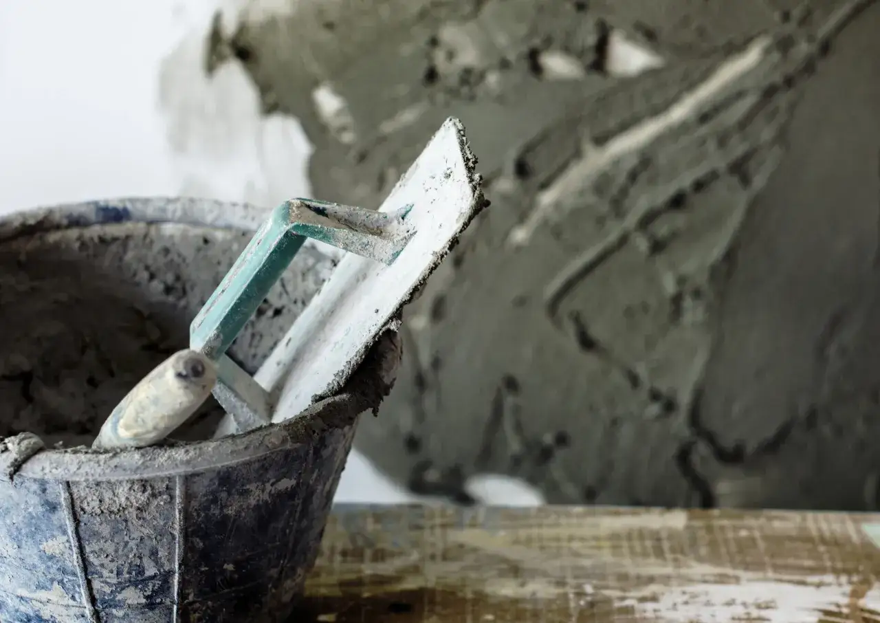 Łopata do tynku cementowo-wapiennego w wiadrze, gotowa do pracy.